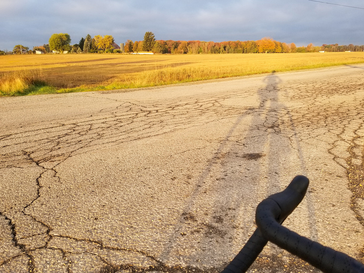 My shadow on across the road in the foreground, some nice autumnal colour in the distance past a field.