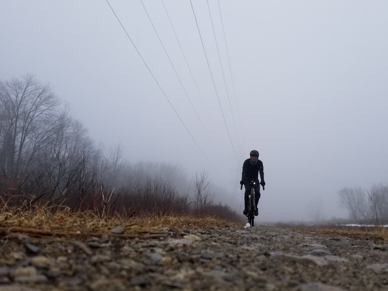 A lone bike rider in the fog with power lines fading into the fog